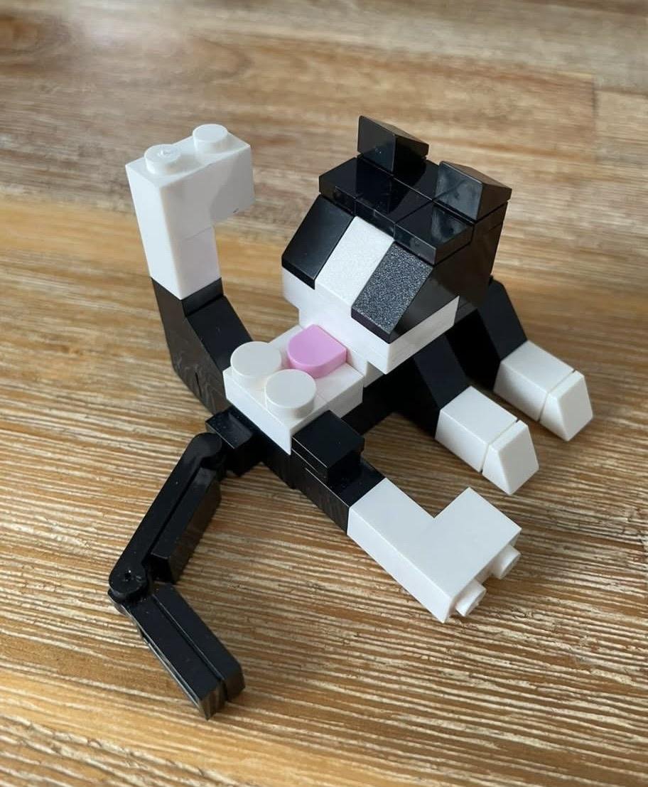 Lego brick construction of a stylized animal figure with black and white blocks, pink accents, and articulated limbs on wooden surface