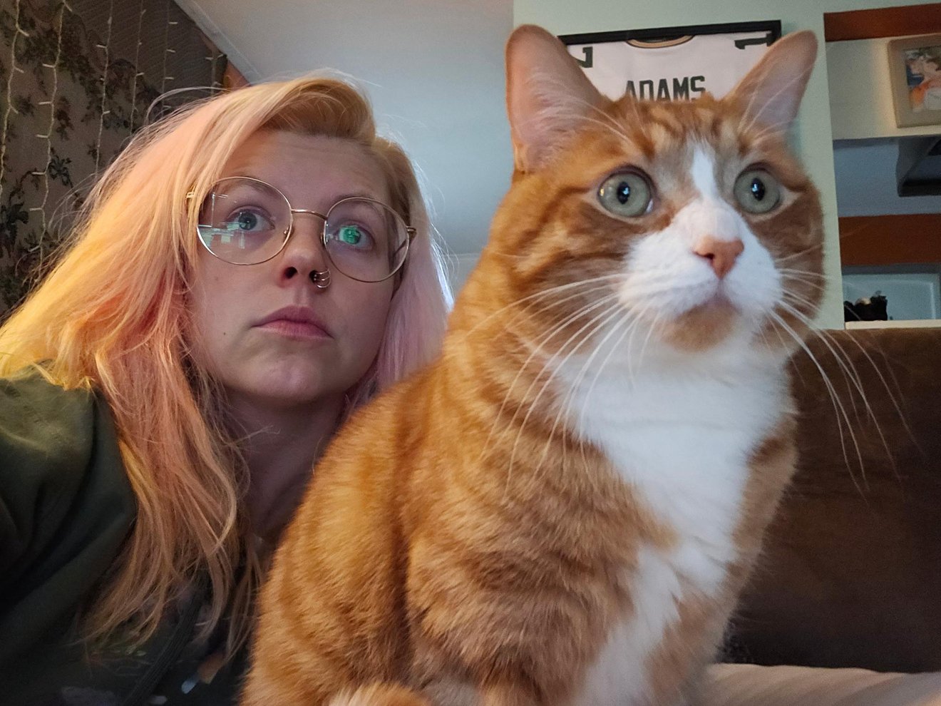 Woman wearing glasses next to an orange and white cat, both making surprised expressions
