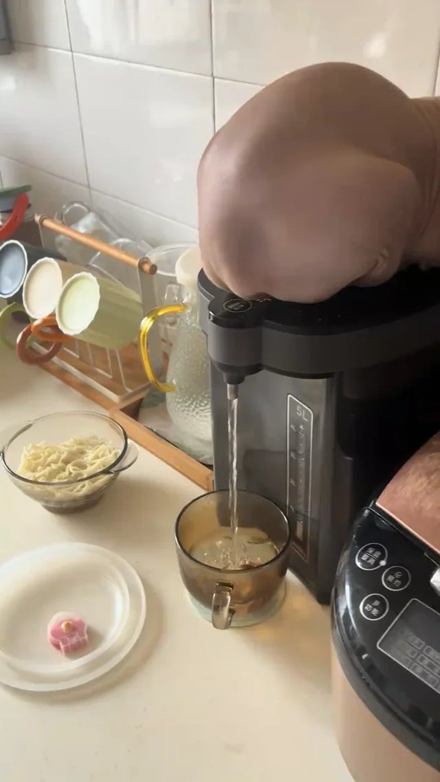 Person's head appearing to pop out of a blender in a kitchen, with ingredients and cooking prep visible nearby