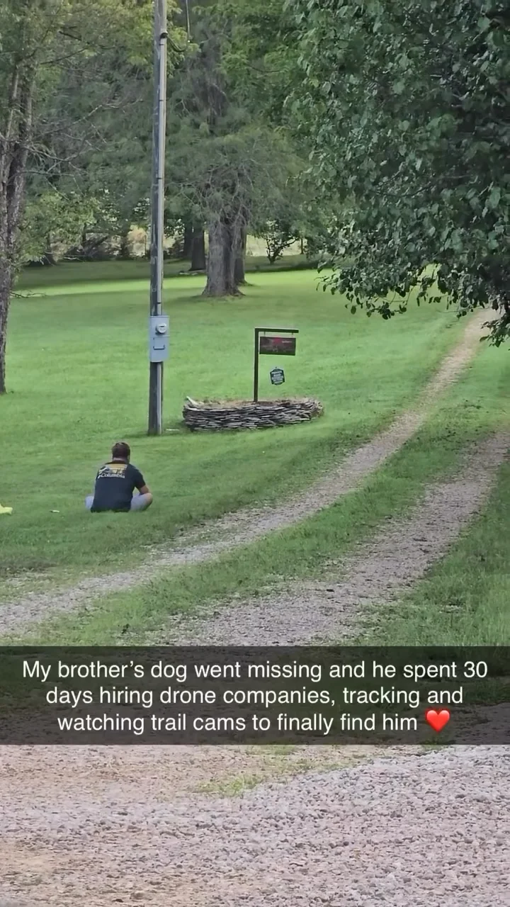 Person sitting on grass near a dirt path with trees, reuniting with their brown dog after 30 days missing