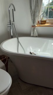 Modern white bathtub with chrome faucet in a bathroom with window and curtains