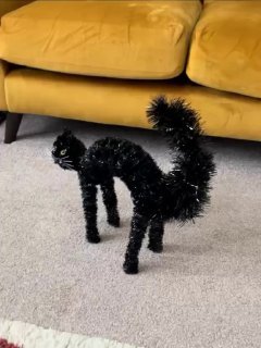 Black poodle standing under a yellow couch on a light carpet, partially hidden