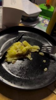 A yellow cat reaching toward scrambled eggs in a dark skillet on a stovetop