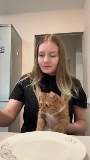 Young woman holding an orange tabby cat in a bathroom, cat looking calm and relaxed